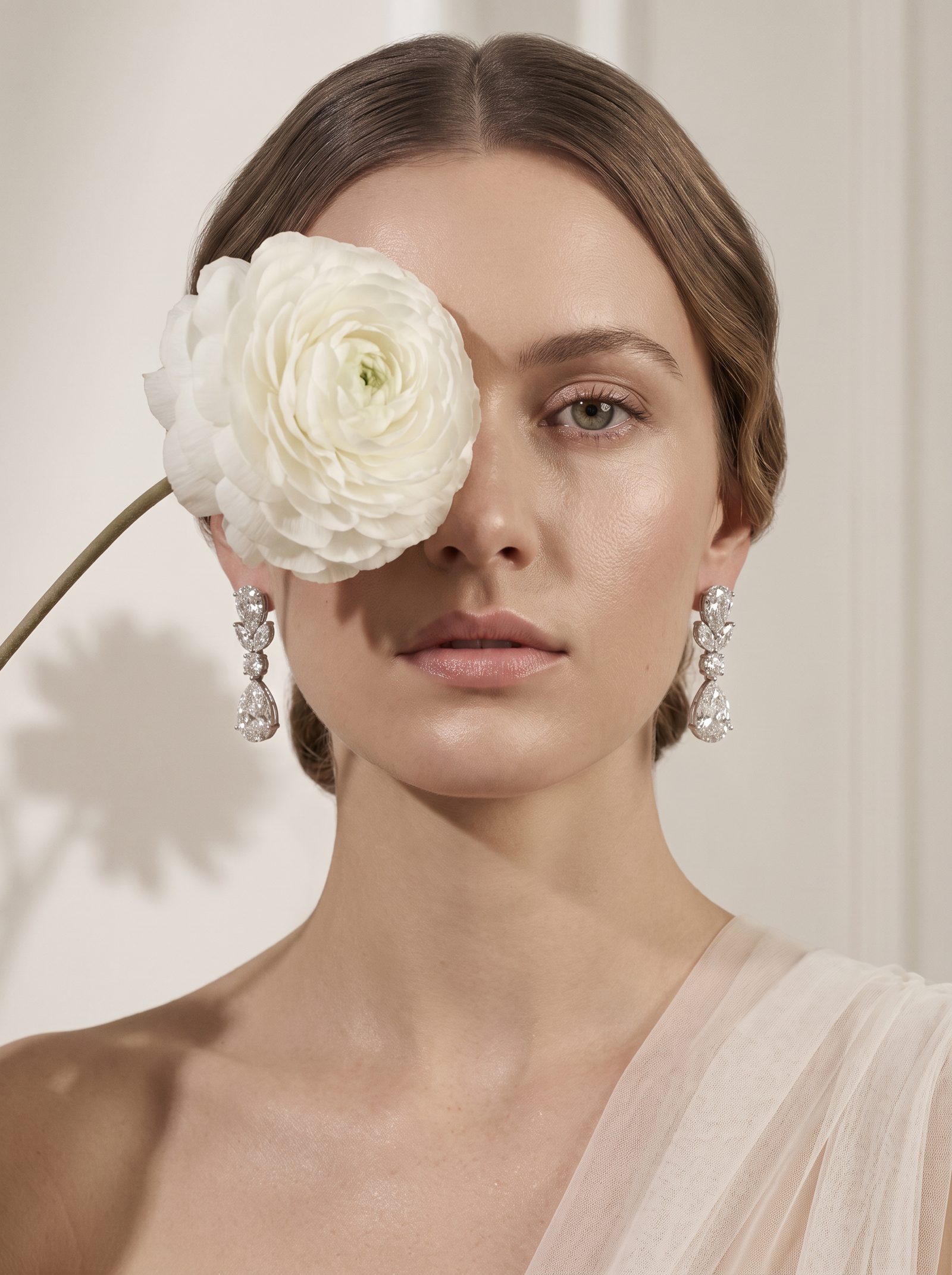 Model holding a white ranunculus, wearing pear and marquise diamond drop earrings in white gold